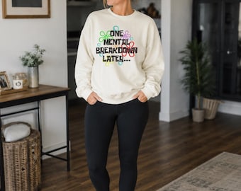 May include: A cream-colored crewneck sweatshirt featuring the black text ONE MENTAL BREAKDOWN LATER surrounded by colorful, outlined flower shapes in blue, green, pink, and yellow, paired with solid black leggings and white athletic sneakers.