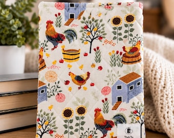 May include: A rectangular quilted fabric cover featuring a cream background with a colorful print of roosters, hens, chicks, blue barns, sunflowers, and apple trees. A white label in the bottom corner reads Made By Thread and Kindness.