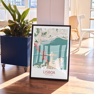 May include: A framed vertical wall art print featuring a stylized map of Lisbon, Portugal. The illustration depicts the 25 de Abril Bridge in red, the Christ the King statue in beige, and the Tagus River in teal, with the text LISBOA at the bottom.