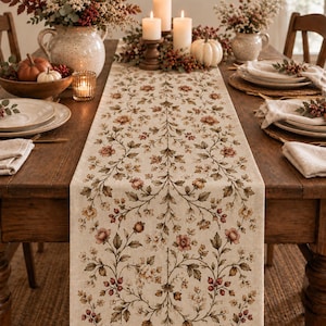 May include: A rectangular table runner featuring a repeating botanical pattern of muted pink flowers, green leaves, and small red berries on a light beige fabric background, centered on a wooden dining table with place settings and candles.