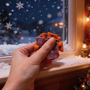 May include: A multi-faceted orange geometric fidget toy with purple glitter triangular faces. Each triangular face features a gold number, including 02 and 11, printed on the surface. The object is constructed from several connected orange plastic segments.
