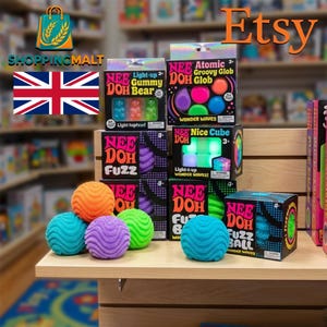 Puede incluir: Una colección de juguetes sensoriales Nee Doh que incluye varias cajas y pelotas texturizadas sueltas. Las cajas muestran marcas como Gummy Bear, Atomic Groovy Glob, Nice Cube y Fuzz Ball. Se exhiben pelotas sueltas en naranja, turquesa, morado y verde.