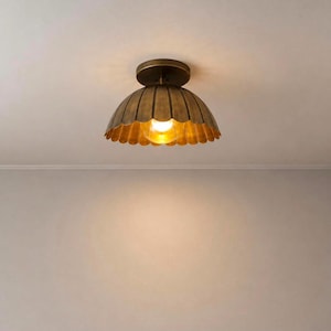 May include: A flush mount ceiling light fixture featuring a dome-shaped metal shade with a scalloped edge and a brushed brass finish. The light emits a warm, glowing light from a single central bulb, casting soft illumination downward.