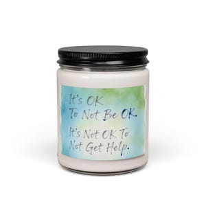 Könnte beinhalten: Ein weißes Kerzenglas mit schwarzem Deckel. Das Etikett zeigt den Text "It's OK To Not Be OK. It's Not OK To Not Get Help." vor einem Aquarellhintergrund in Blau und Grün.