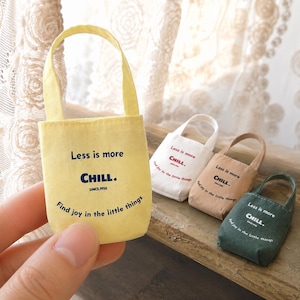 Miniature canvas tote bag shown in hand with yellow, white, beige, and green color options in the backg