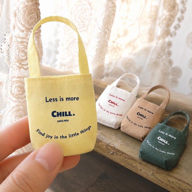 Miniature canvas tote bag shown in hand with yellow, white, beige, and green color options in the backg