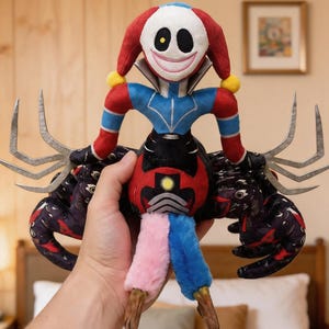 May include: A plush toy featuring a white face with a wide smile, red and blue jester-style headgear, and multiple spider-like limbs. The body has a black and red patterned torso, blue and pink legs, and silver-colored claw-like appendages.
