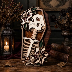 May include: A layered wooden wall art piece shaped like a coffin, featuring a light-colored skeleton silhouette against a dark wood background. The design is accented with multi-layered floral motifs in cream, dark red, and green tones.