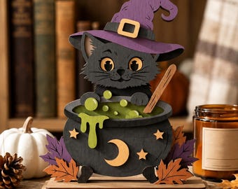 May include: A layered wooden cutout decoration featuring a black cat wearing a purple witch hat, sitting inside a black cauldron filled with green bubbling liquid. The cauldron is decorated with a crescent moon and stars, surrounded by autumn leaves.