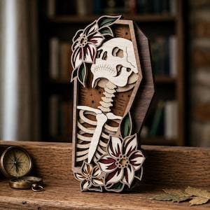 May include: A multi-layered wooden wall art piece shaped like a coffin, featuring a carved skull and ribcage skeleton design. The artwork is decorated with layered floral motifs in shades of deep red, green, and natural wood tones, with small star accents.