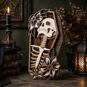 May include: A layered wooden wall art piece shaped like a coffin, featuring a light-colored skull and ribcage skeleton design. The coffin is decorated with dark-toned, multi-layered floral accents in shades of deep red, green, and cream.