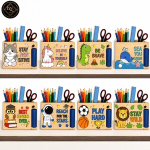 Op de afbeelding: Acht bureau-organizers van licht hout, elk met een kleurrijk figuur en tekst. De ontwerpen bevatten een kat met 'STAY PAW SITIVE', een eenhoorn met 'BELIEVE IN YOURSELF', een dinosaurus met 'BE BRAVE', een walvis met 'SEA YOU SOON', een uil met 'BEST TEACHER EVER', een astronaut met 'REACH FOR THE STARS', sportballen met 'PLAY HARD' en een leeuw met 'STAY WILD'. Elk exemplaar bevat potloden, een schaar en een liniaal.