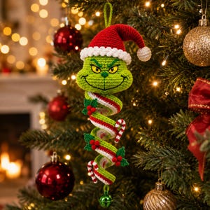 May include: A crocheted hanging ornament featuring a green character head wearing a red and white Santa hat. Below the head is a spiral body made of green, white, and red yarn, decorated with small holly leaves and berries, ending in a green bell.
