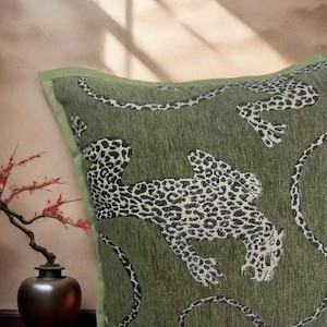 May include: Green decorative pillow with a leopard print design. The pillow features a green background with black and white leopard patterns. The pillow has a green border and is likely made of a woven fabric.