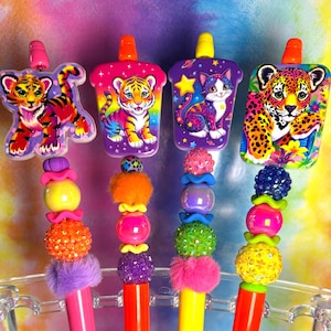 May include: Four pens with colourful plastic barrels in pink, orange, yellow, and orange. Each pen features a decorative topper with animal illustrations and a stack of textured, multi-coloured beads including fuzzy, glittery, and smooth spheres.