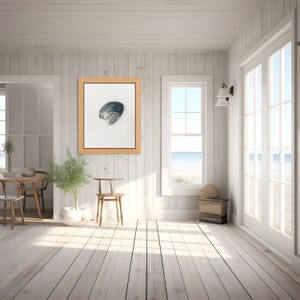 May include: A framed wall art piece featuring a detailed illustration of a single dark blue and grey seashell centered on a white background, enclosed within a light wood frame, displayed on a white vertical paneled wall in a bright room.