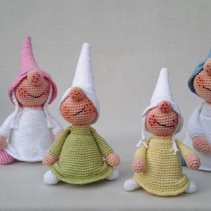 May include: Four handmade crochet dolls with pointed hats and round noses. The dolls feature peach-colored faces with stitched smiles and rosy cheeks. They wear dresses in white, olive green, and yellow, with hats in pink, white, and blue colors.