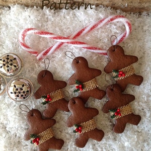 May include: Six gingerbread man ornaments with burlap ribbon and red berries. The ornaments are on a white background with a red and white candy cane.