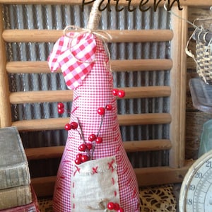 May include: A red and white gingham pear-shaped pillow with a burlap pocket and red berries. The pillow is decorated with a red and white gingham heart and the text "Kokomo Lane Primitives Pattern".