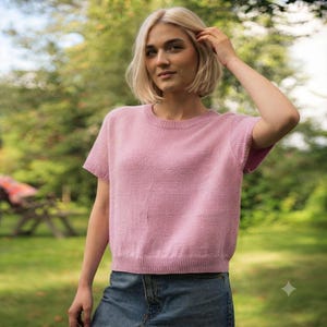 Peut inclure: Un pull à manches courtes en tricot rose clair doté d'une encolure ronde et d'un ourlet côtelé. Le vêtement est confectionné avec un motif en tricot fin et texturé, présentant une coupe décontractée, associé à un jean bleu avec une couture visible.
