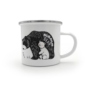 Peut inclure: Mug en émail blanc avec une illustration en noir et blanc d'une maman ours et d'un ourson. Les mots "Mama Bear" sont écrits sur la tasse. Elle a un bord argenté et une anse blanche.