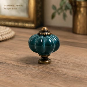Può includere: Un pomello per mobili in ceramica verde ottanio scuro con design a forma di zucca e base in ottone anticato. Il testo "Handmade Ceramic Antique Brass" è visibile nell'angolo in alto a sinistra. Il pomello presenta una finitura lucida.