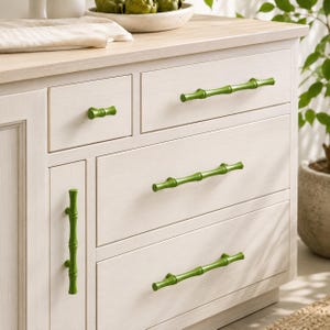 May include: A light-colored wooden cabinet featuring several green drawer pulls and handles designed to resemble bamboo stalks. The hardware includes one small knob, one vertical handle, and three horizontal handles, all in a vibrant green finish.