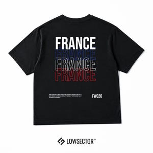 Pu&ograve; includere: Una t-shirt nera a maniche corte con la parola FRANCE stampata quattro volte in un design sovrapposto con contorni bianchi, blu e rossi. Sotto il testo, una piccola scritta bianca riporta FWC26 accanto a un paragrafo sulla storia del calcio.