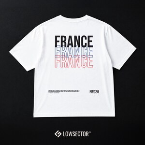Pu&ograve; includere: Una t-shirt bianca a maniche corte con la parola FRANCE stampata tre volte in nero, blu e rosso. Sotto, un piccolo testo nero fornisce informazioni storiche accanto al testo FWC26. Il nome del marchio LOWSECTOR &egrave; stampato in basso.