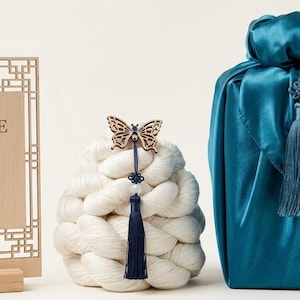 May include: A rectangular wooden sign with the text IRENE and Korean characters, a white yarn bundle topped with a wooden butterfly ornament and a dark blue tassel, and a teal satin fabric wrap featuring a matching dark blue decorative tassel.