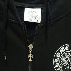 May include: Black zip-up hoodie with a silver cross-shaped zipper pull. The hoodie features a white patch with a circular emblem and text. The right side of the hoodie has a white emblem with the word "Chrome".