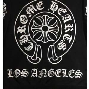 May include: Black sweatshirt with a large white graphic. The graphic features a circular design with the words "Chrome Hearts" and "Los Angeles" in a gothic font. A floral cross is in the centre of the circle.