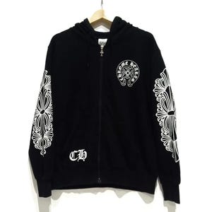 May include: Black zip-up hoodie with white ornate designs on the sleeves and a circular emblem on the chest. The hoodie features the letters "CH" on the front and a silver zipper.