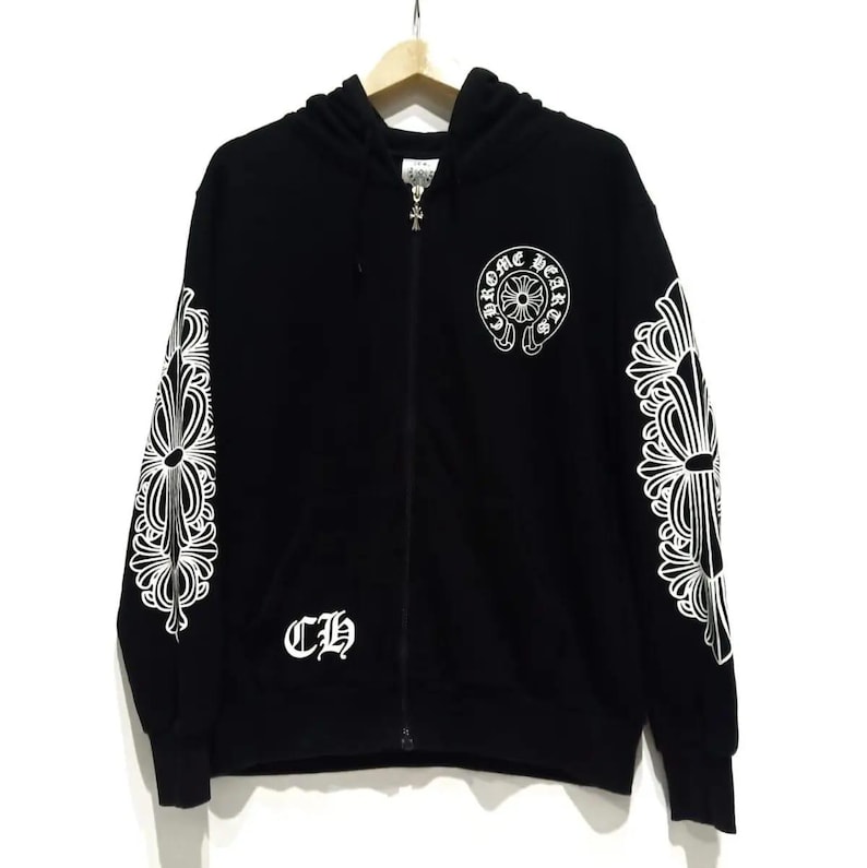 May include: Black zip-up hoodie with white ornate designs on the sleeves and a circular emblem on the chest. The hoodie features the letters "CH" on the front and a silver zipper.