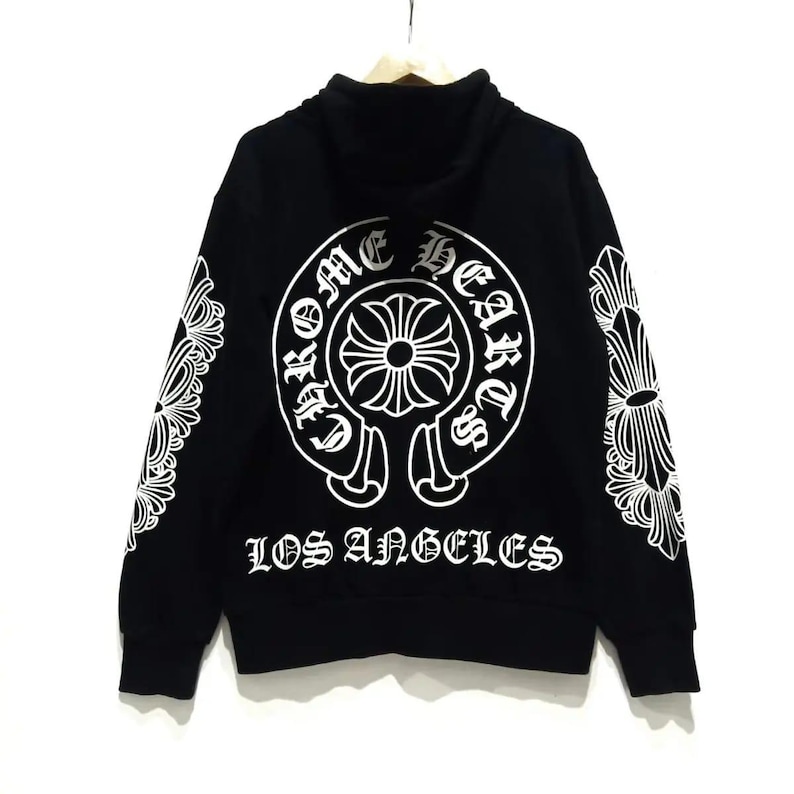 May include: Black hoodie with a high collar and white graphic designs. The back features a large circular emblem with the words "Chrome Hearts" and "Los Angeles". White floral designs are on the sleeves.