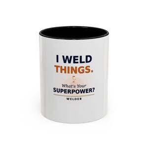 May include: A white ceramic mug with a black interior. The mug features the text "I WELD THINGS." in navy blue, with "THINGS." in orange. Below, it reads "What's Your SUPERPOWER? WELDER."