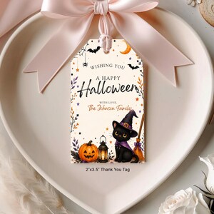 Op de afbeelding: Een rechthoekig papieren label met een lichtcrème achtergrond, voorzien van een zwarte kat met een paarse heksenhoed, een oranje pompoen, een lantaarn en een bezem. Tekst: Wishing you a happy Halloween with love, The Johnson Family. 2"x3.5" label.