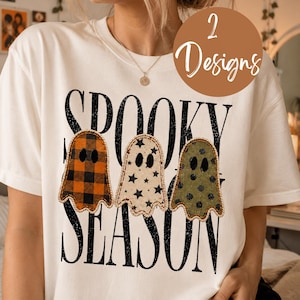 May include: A white t-shirt featuring the black text SPOOKY SEASON and three ghost illustrations. The first ghost has an orange and black plaid pattern, the second is cream with black stars, and the third is olive green with black polka dots.