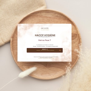 Peut inclure: Une carte blanche avec le texte "HACCP HYGIÈNE" et "Vrai ou Faux ?" est posée sur une assiette en bois. La carte comprend également le texte "MODULE 1/3" et d'autres textes en français. L'assiette est sur une surface beige.