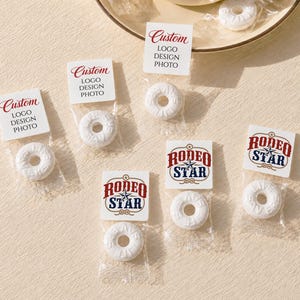 May include: Several white ring-shaped candies individually wrapped in clear plastic pouches. Each pouch features a white square label with either the text Custom LOGO DESIGN PHOTO in red and black or the text RODEO STAR with a blue star graphic.