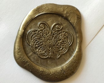 Op de afbeelding: Een gouden zegellak met een gedetailleerd vlinderontwerp.