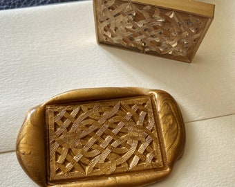 Op de afbeelding: Een gouden waszegel met een gedetailleerd Keltisch knoopontwerp. De zegel is gemaakt van was en heeft een glad, glanzend oppervlak.