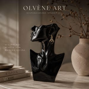 Può includere: Un espositore a busto nero lucido con una silhouette liscia e astratta di testa e collo umani. La scultura è decorata con un singolo orecchino geometrico color oro con piccole pietre trasparenti. Il testo recita OLVÈNE ART, SCULPTURAL ELEGANCE, TIMELESS BEAUTY, SCULPTURAL BEAUTY FOR MODERN LIVING.