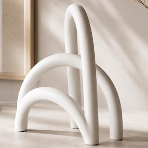 Peut inclure: Une sculpture abstraite en céramique blanche avec des formes arquées et incurvées. La sculpture a une finition mate et repose sur une surface de couleur neutre. Le design est minimaliste et moderne, adapté à la décoration intérieure.