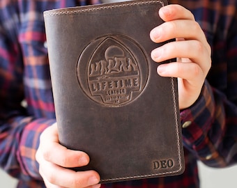 May include: A dark brown leather notebook cover with visible stitching along the edges. The front features a circular embossed logo with a mountain landscape, the text "LIFETIME LEATHER", "SAN TAN VALLEY", "AZ", and the letters "DEO" at the bottom.