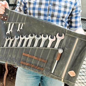 May include: A gray canvas tool roll with a variety of wrenches and a ratchet. The roll has brown leather accents and a zipper closure. The tools are neatly organized in individual pockets.