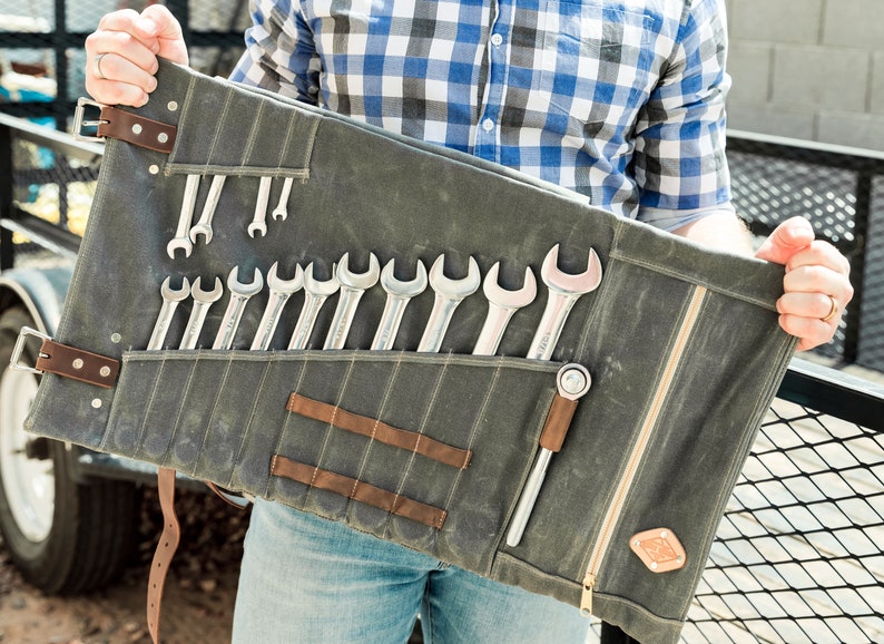 May include: A gray canvas tool roll with a variety of wrenches and a ratchet. The roll has brown leather accents and a zipper closure. The tools are neatly organized in individual pockets.