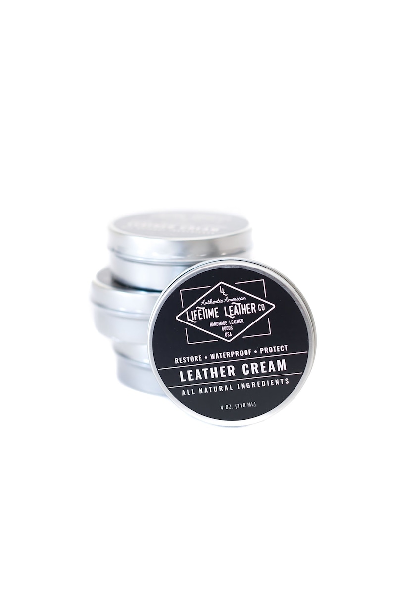 May include: A stack of silver tins with a black label that reads "Authentic American Lifetime Leather Co. Handmade Leather Goods USA. Restore Waterproof Protect Leather Cream All Natural Ingredients 4 oz. (118 ml)"