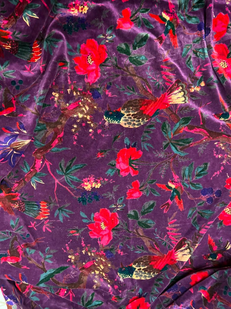 May include: A deep purple velvet fabric featuring a repeating pattern of vibrant red flowers, dark green leaves, and multi-colored birds with red, yellow, and blue plumage perched on brown branches throughout the textile surface.