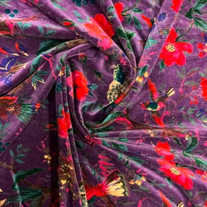 May include: A deep purple velvet fabric featuring a vibrant floral and bird pattern. The design includes bright red flowers, green leaves, and multi-colored birds perched on branches, creating a rich, textured surface with soft folds.
